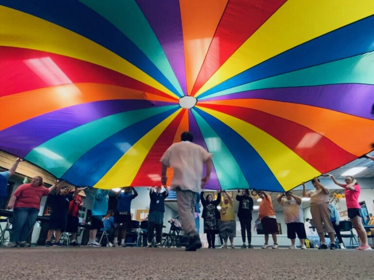 Individuals participate in Goodwill Week 2024 by playing with a large colorful parachute.
