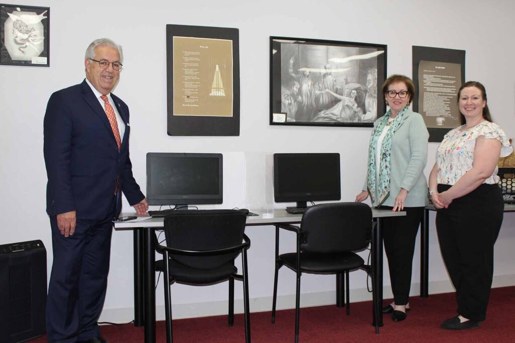 Three individuals stand around desk of computers.