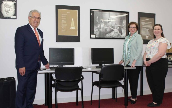 Three individuals stand around desk of computers.