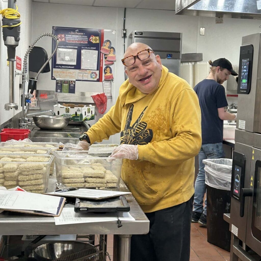 A man wearing a yellow sweatshirt works in the kitchen of Chili's