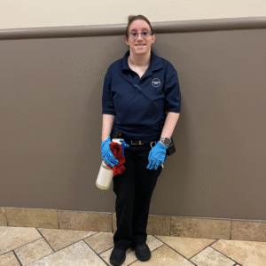 A woman stands in a hallway while holding janitorial supplies