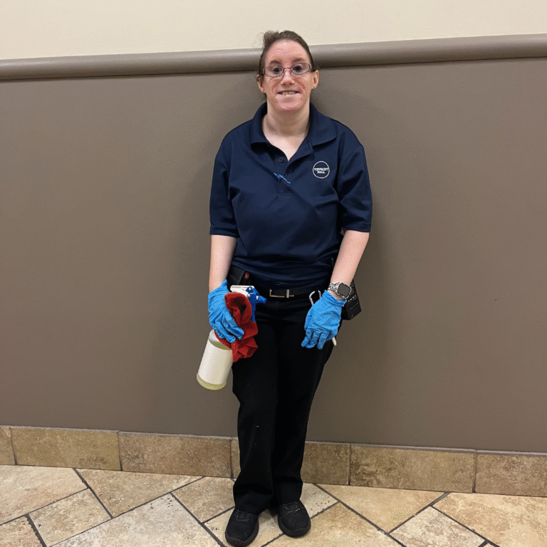 A woman stands in a hallway while holding janitorial supplies