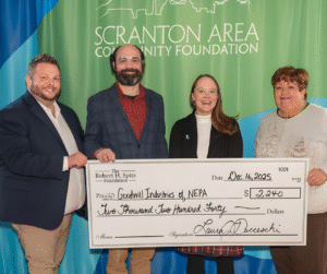A group of four individuals gather around a large check awarded to Goodwill