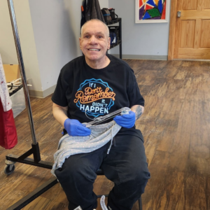 A smiling man is holding a piece clothing while working at Goodwill Industries of Northeastern Pennsylvania.