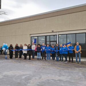A group of individuals gather in front of a new Goodwill retail store and cut a ribbon to celebrate the grand opening.