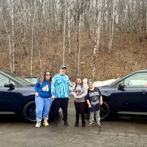Individuals pose in front of two new vehicles in an outdoor setting